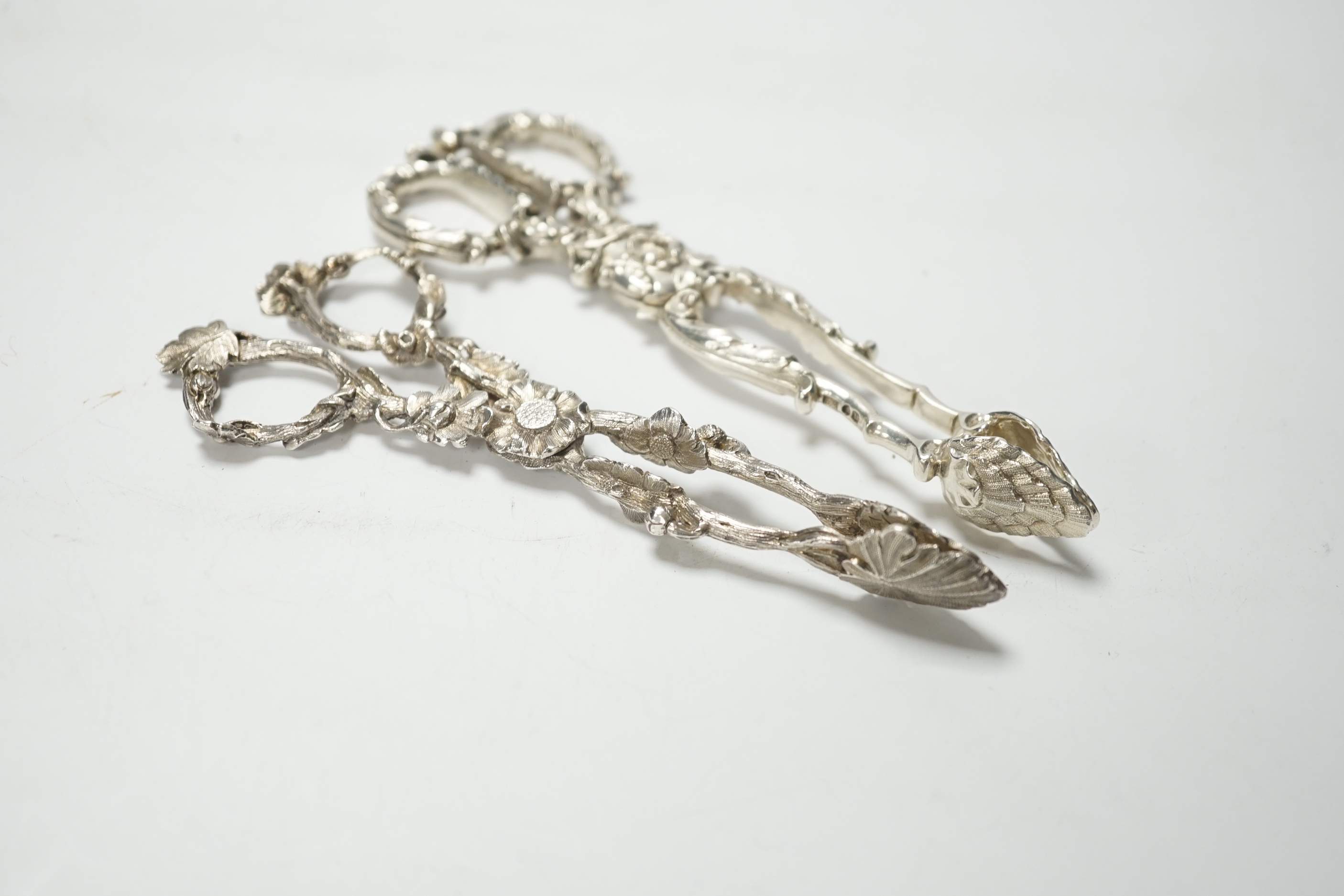 A pair of Victorian cast silver sugar tongs, of foliate design, by George Adams, London, 1871, 14.2cm and a pair of William IV cast silver sugar tongs, by Theobalds & Bunn, London, 1835, 15.4cm, 102 grams.